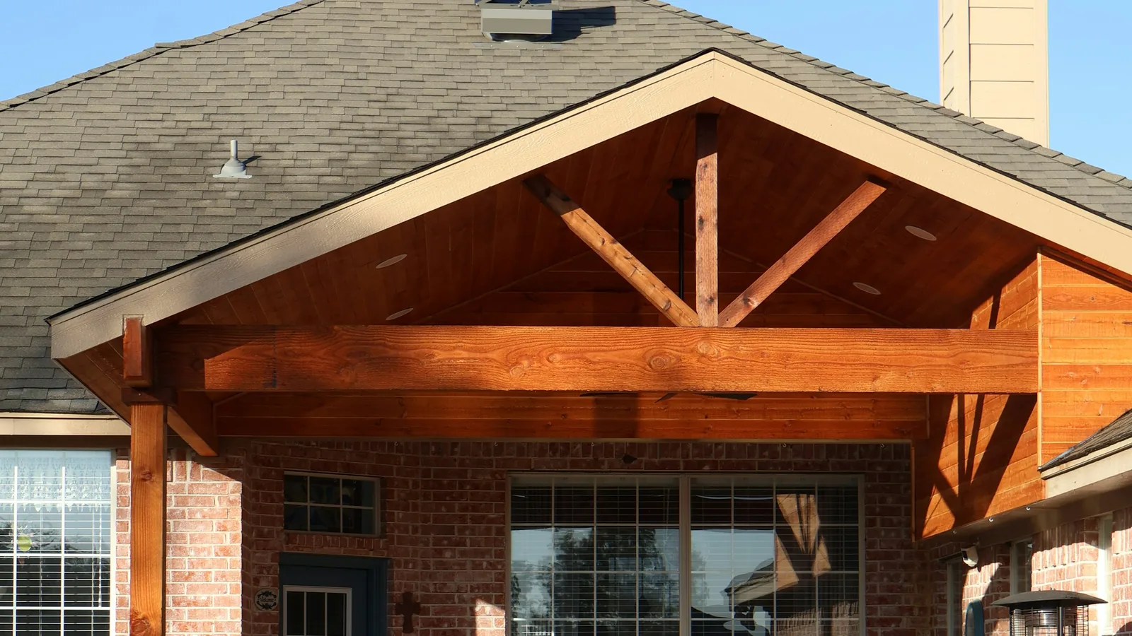 Covered patio with a timber-framed roof on a brick home